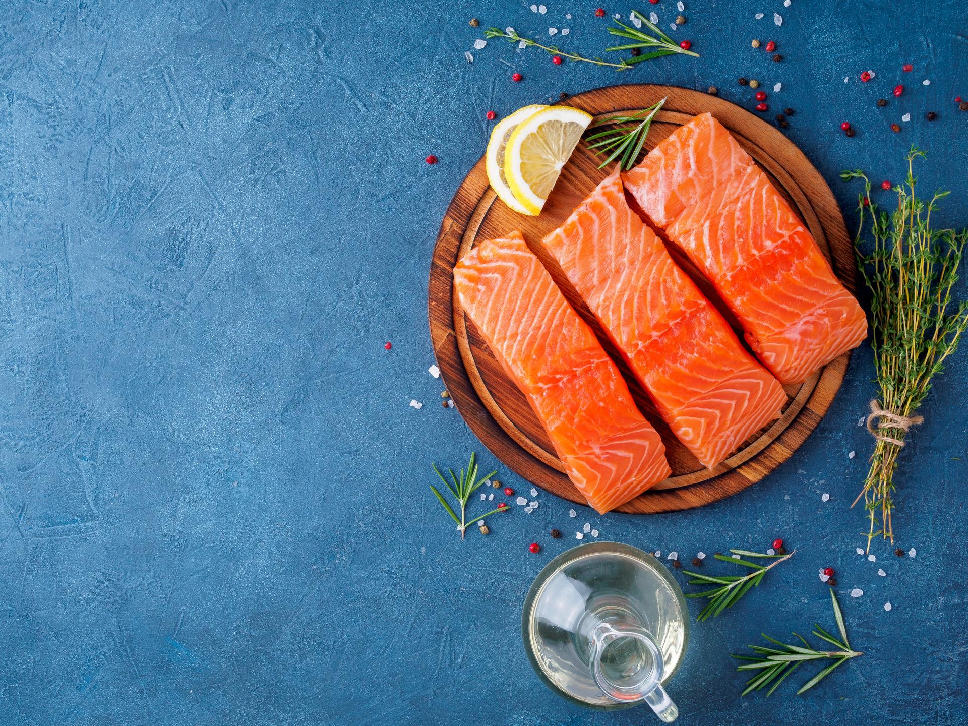 Food background, sliced portions large salmon fillet steaks on chopping board on dark blue concrete table, copy space, top view